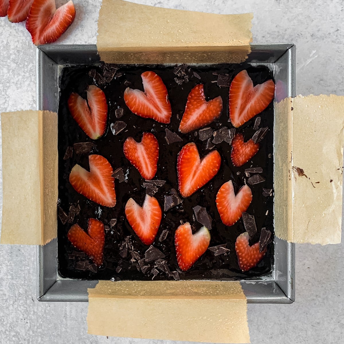 brownie batter in pan with sliced strawberries on top.