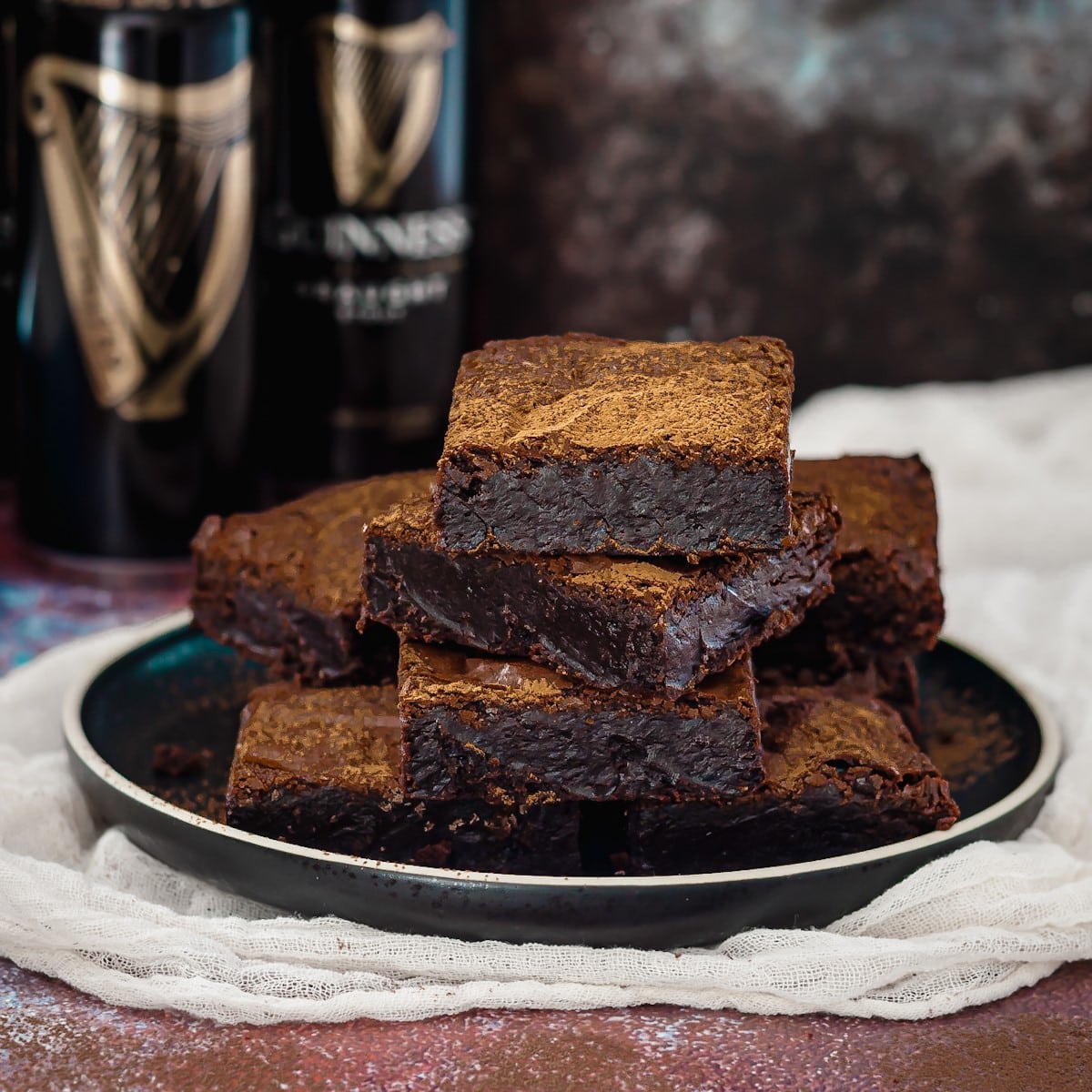 Guinness stout chocolate brownies stacked on a plate in front of guinness beer cans.