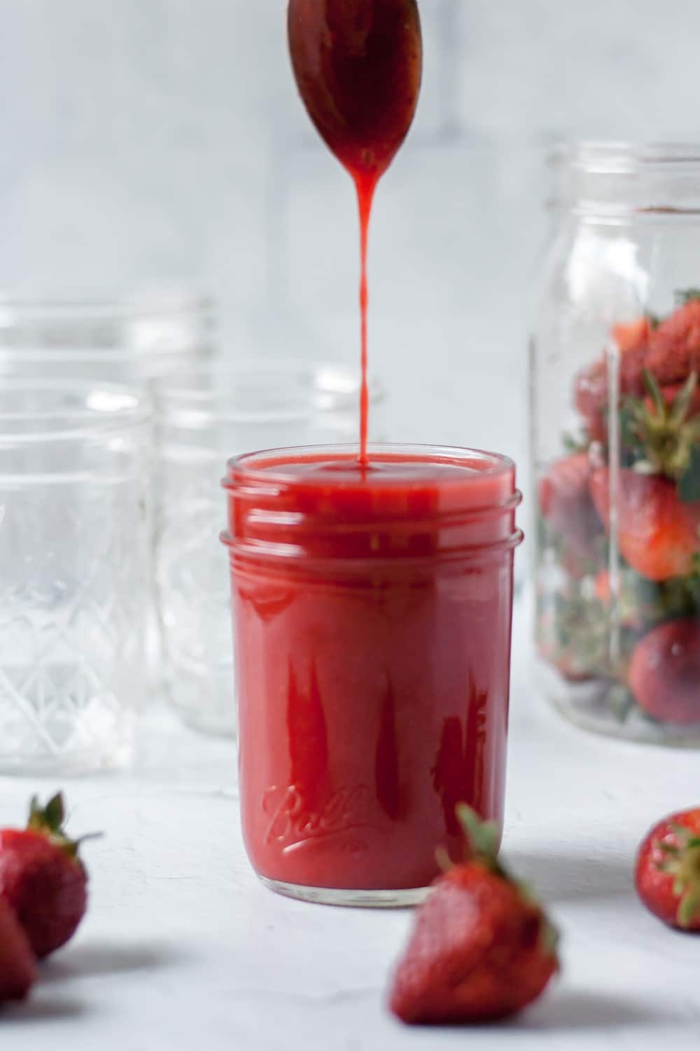 Spoon dripping strawberry coulis into glass mason jar.