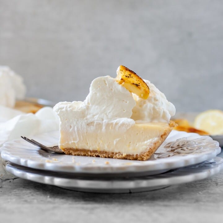 Slice of old fashioned lemon pie on stacked plates with whipped cream and a lemon slice.