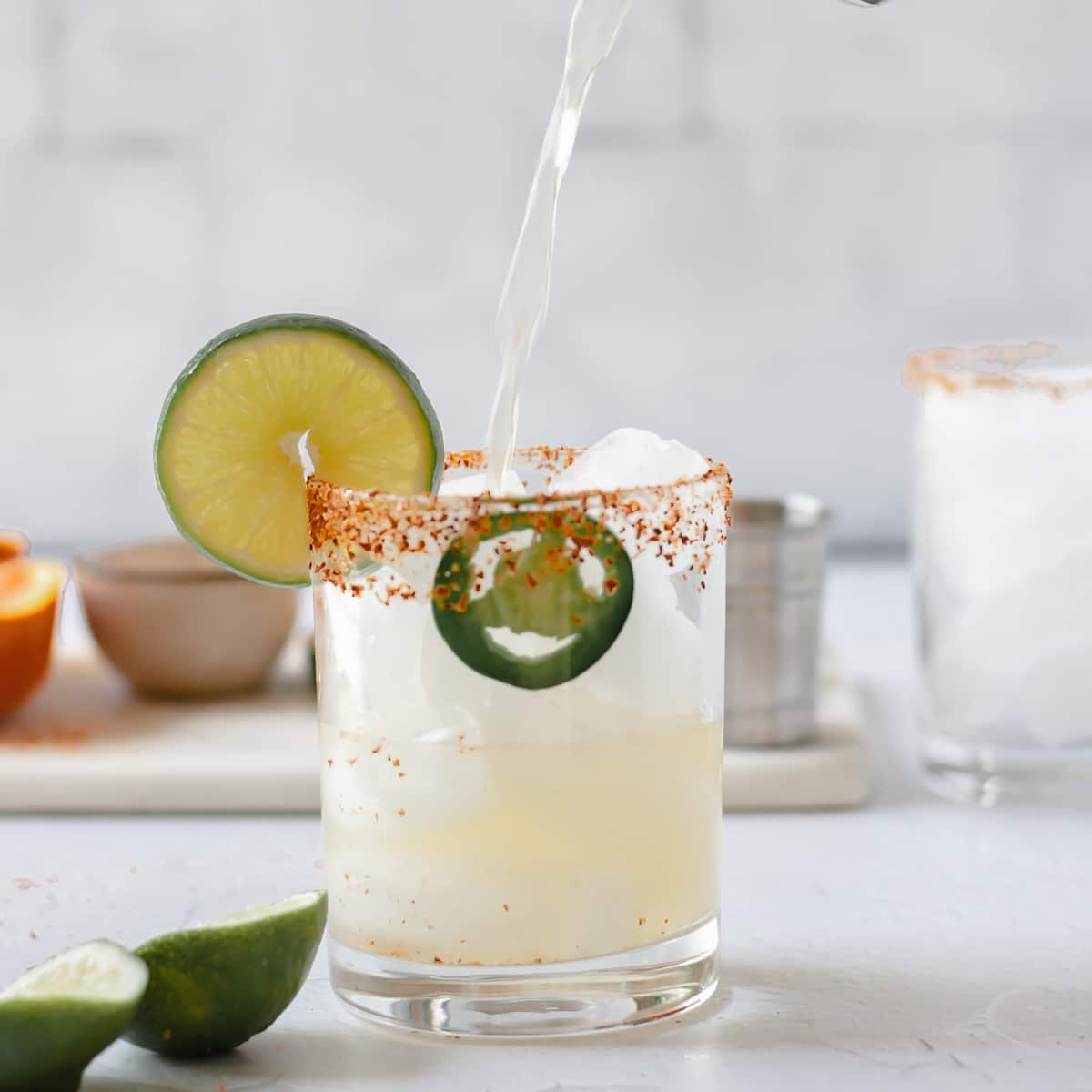 skinny spicy margarita pour in a glass with a jalapeno and a lime