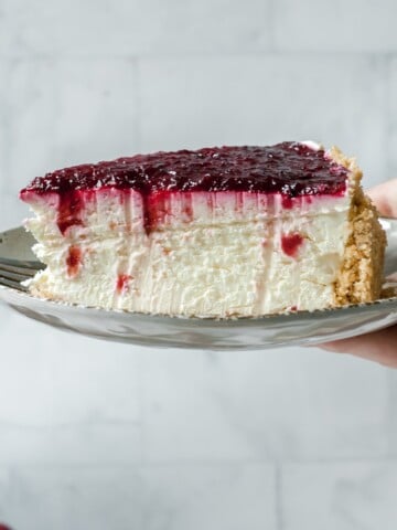Side view of slice of cherry cheesecake on a plate held in a hand.