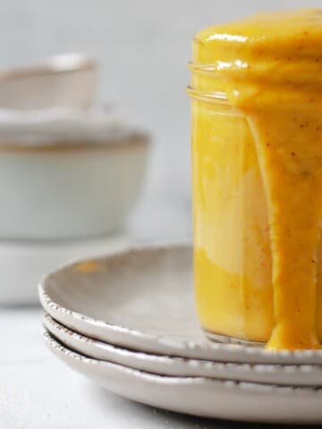 Carolina gold mustard bbq sauce in a mason jar on a plate stack.