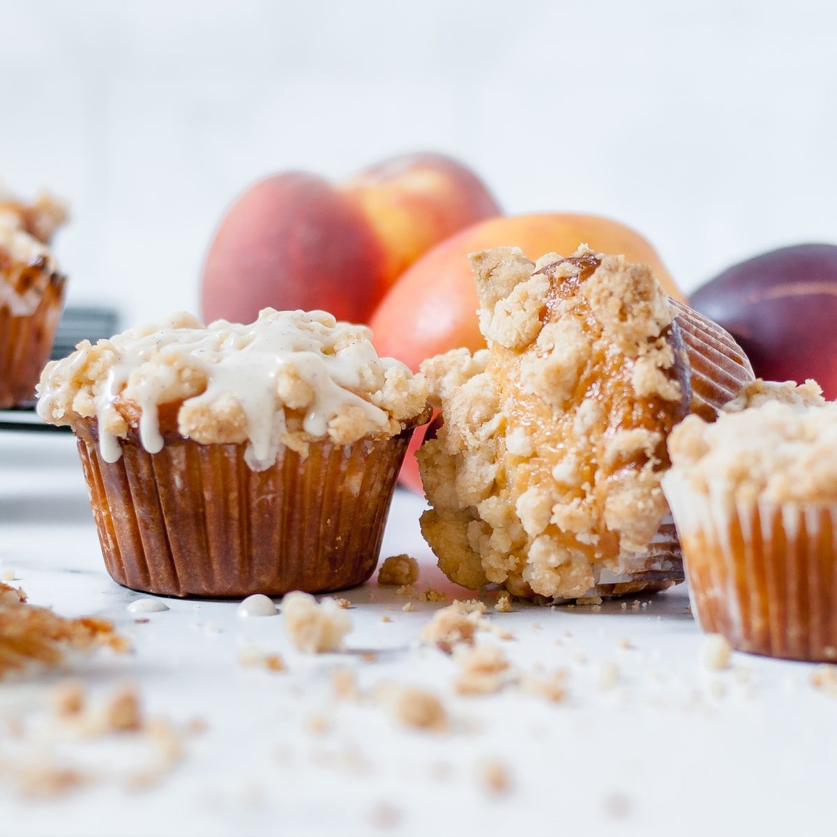 Peach muffins with vanilla bean glaze, streusel crumbs and peaches in the background.