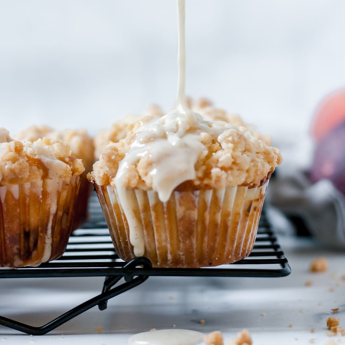 Peach muffins being drizzled with vanilla bean glaze.