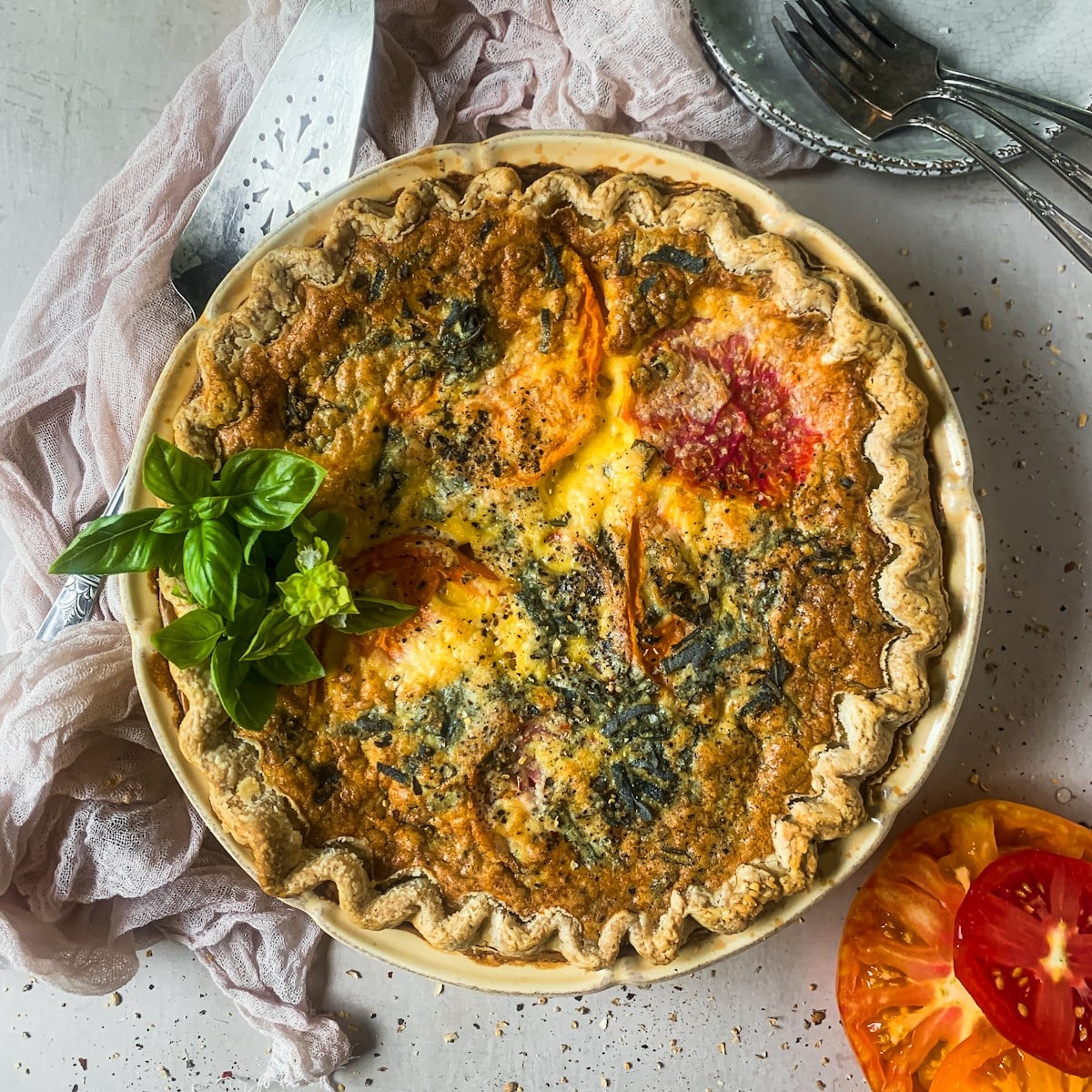 Whole tomato quiche in a pie plate with tomatoes and basil.