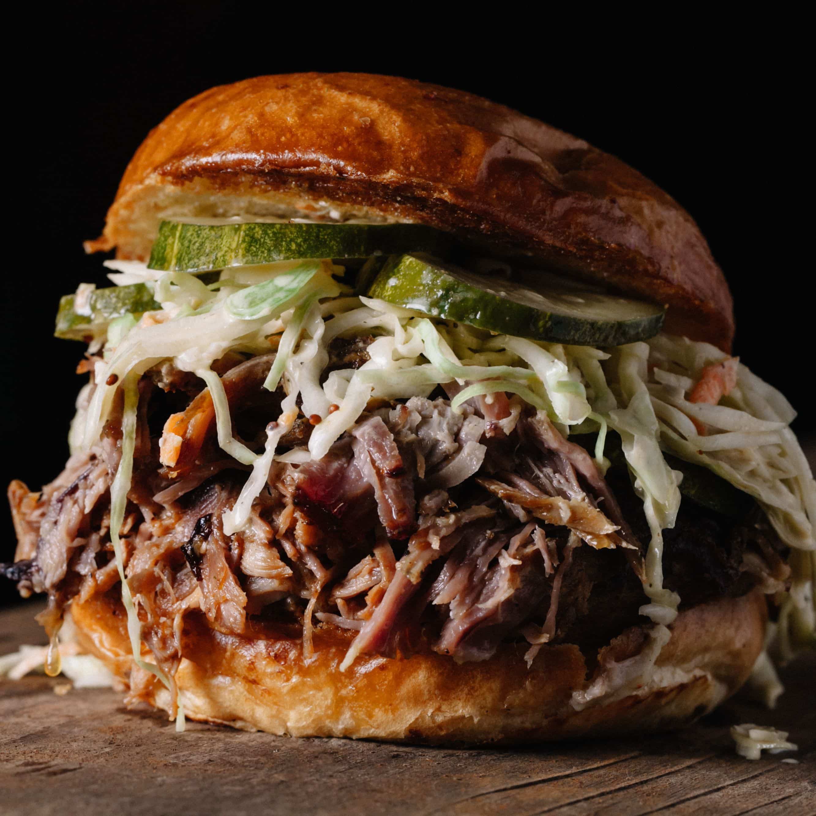 Closeup of a pulled pork sandwich with slaw and pickles